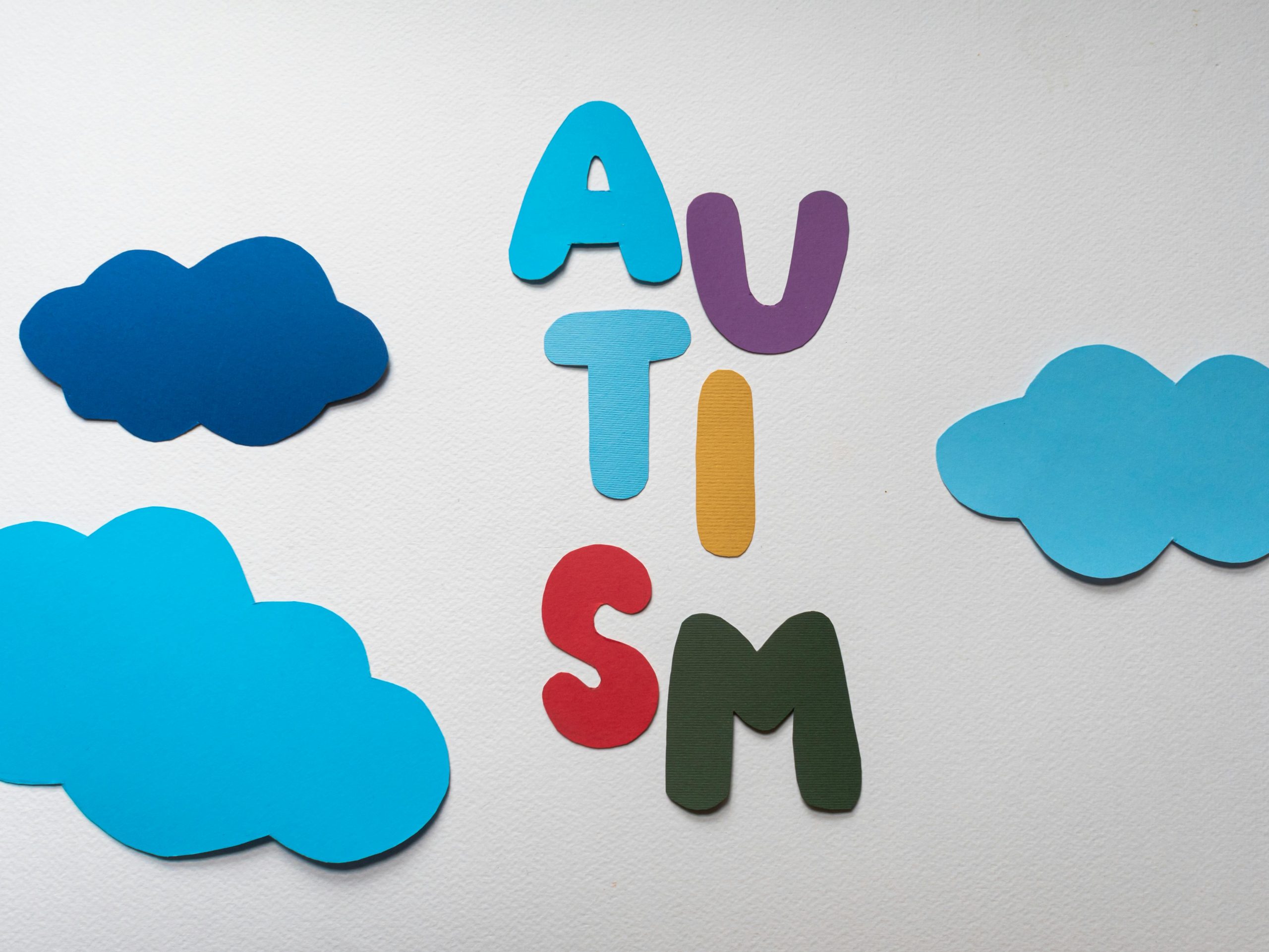 Vibrant letters spelling 'AUTISM' surrounded by blue paper clouds on a white background.