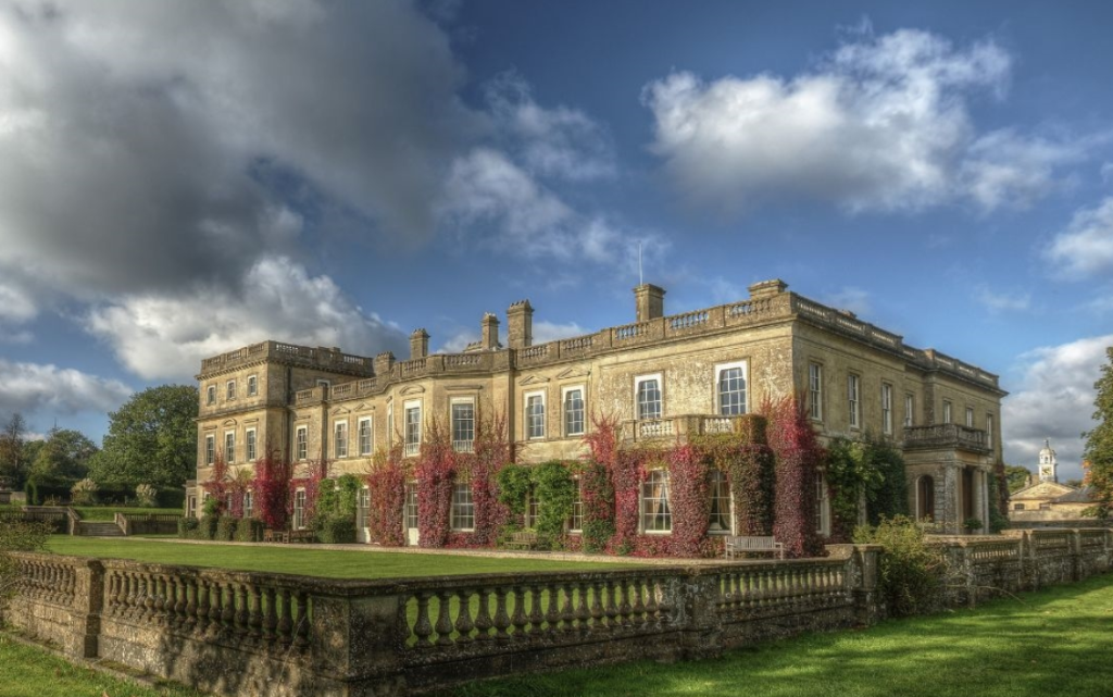 Hartham Park country house with red ivy beneath a blue and cloudy sky, with lawns in the foreground